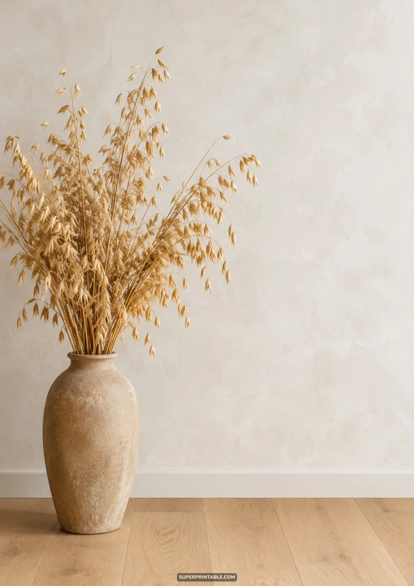 Beige ceramic urn filled with tall dried oat sheaves resting on light hardwood flooring against a neutral wall